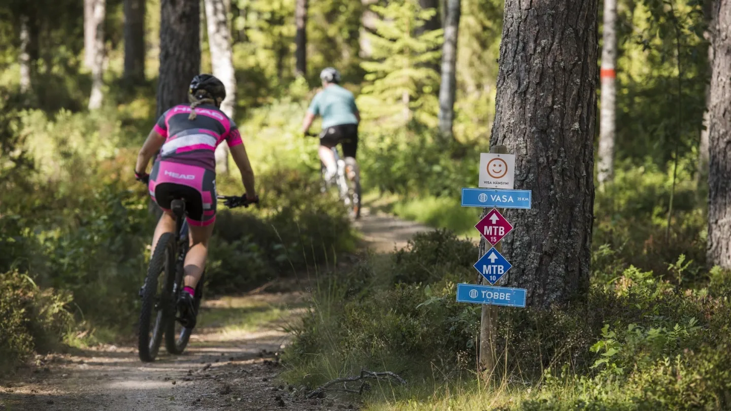 Två personer cyklar på en stig genom skogen på Högbo MTB Arena