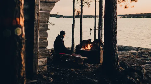 Man sitter vid lägereld vid vatten i skymningen