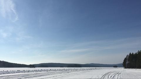 Vintervit öppet landskap över en infrusen sjö en solig daf med blå himmel