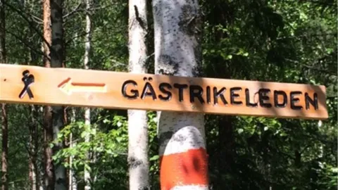 En träskylt i skogen med texten Gästrikeleden