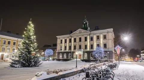 Stor fin vit byggnad vid ett torg med en stor gran en fin vinterkväll med snö