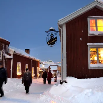 Liten gata med mycket snö som går mellan röda hus en vinterkväll