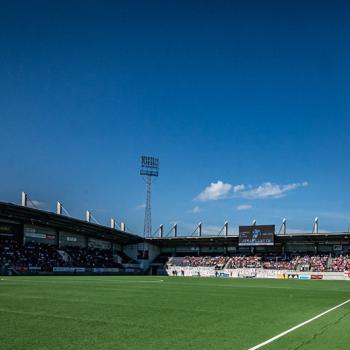 Fotbollsarenan Gavlevallen med en grön tom gräsmatta, publik på läktaren och blå himmel