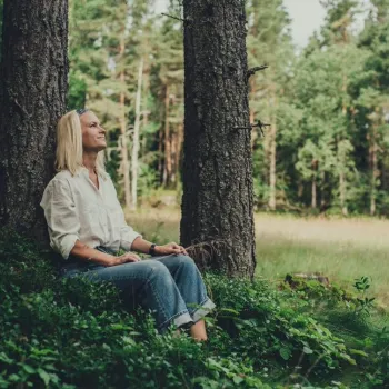 Kvinna vilar mot ett träd i skogen