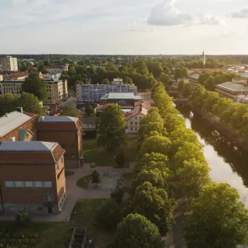 Stor tegelbyggnad inbäddad i grönska vid Gavleån